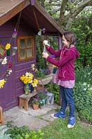 Young girl decorating her playhouse with small vases on string and flowers