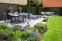 Contemporary suburban garden with copper feature wall, patio with dining furniture and hedging