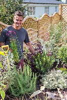 Antony Henn from Garden on a roll by newly planted border of mature plants where plants are placed according to the paper plan for the designed border