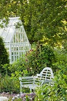 Secluded place with garden bench under a mature English oak, obelisk as support to roses and clematis backed with a conservatory. Design: Carol Bruce