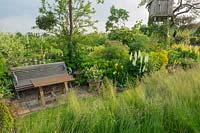 A wooden bench and table is part of the long border with long grass in the wild flower meadow and backing onto the cultivated pear orchards.