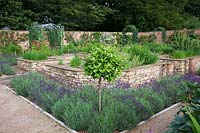 The herb garden in walled kitchen garden with focal point Armillary Sphere by David Harber. Raised beds with herbs including Chives, Mnarda, Rosemary, made of drystone walls surrounded by Lavandula 'Imperial Gem'.   Steel arches with Sweet Peas and half standard Bay tree. 