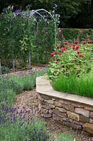 The herb garden in walled kitchen garden with raised beds made of drystone walls surrounded by Lavandula 'Imperial Gem'. Steel arches with Sweet Peas and Monarda 'Gardenview Scarlet' - Bergamot and Chives. 