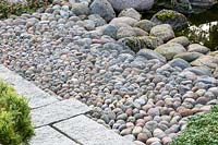 Details of the materials used in an Asian garden: densely stacked pebbles as transition from the boulders at the water edge to the flagstone paved garden path.