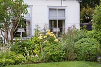 Border at the front of the house includes Syringa vulgaris, Rosa 'Golden border', Foeniculum 'Purpureum', box topiary, lychnis coronaria 'Alba', and Geranium pratense 'Mrs Kendall Clark'. Hetty van Baalen garden, The Netherlands