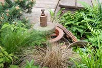 Sculptural rusty cogs with planting of ferns and bronze Carex - Industrial Decay in Walker's Wharf Garden supported by Doncaster Deaf Trust - RHS Chelsea Flower Show 2017 