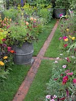 The BBC Radio 2 Feel Good Gardens, The Anneka Rice Colour Cutting Garden. The garden beds are divided by a narrow brick path running between Geum 'Mai Tai', Papaver dubium subsp. leqoqii and Calendula of cinalis 'Indian Prince' complete with a galvanised planter - RHS Chelsea Flower Show 2017