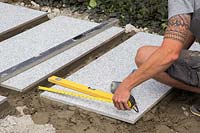 Making a mixed material patio  - man measuring gap between large porcelain slabs to ensure there is correct spacing