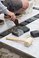 Making a mixed material patio  - man infilling space between large porcelain slabs with dark granite setts