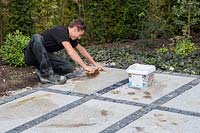 Making a mixed material patio - man using jointing compound on patio with mix of large porcelain slabs and granite setts
