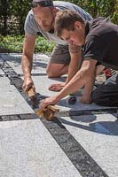 Making a mixed material patio - men using jointing compound on patio with mix of large porcelain slabs and granite setts