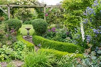 View to pergola with bird bath. Ilex crenata topiary and box edging. Herbaceous perennials including alliums, alchemilla, astrantia and irises. Shrubs including ceanothus, roses and magnolia