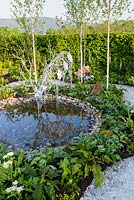 Metal stag sculpture drinking from a pond in glade of silver birches with planting including Aquilegia, ferns, Pulmonaria, hostas and Brunnera - Buckfast Abbey Millennium Garden, RHS Malvern Spring Festival 2017 