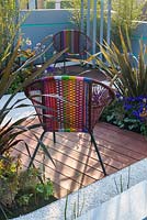 Colourful garden chairs with planting of bamboo, phormium and Pericallis x hybrida 'Senetti Deep Blue'- Ocean Garden, RHS Malvern Spring Festival 2017 