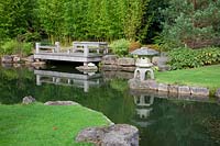 A Japanese style zen garden with oak deck jetty overlooking pond,  Bamboo, Viburnum davidii, Pinus and  stone lantern ornament - Brightling Down farm