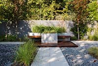 Mixed planting of Kniphofia flamenco, Miscanthus sinensis 'Ferner Osten', Molinia caerulea 'Karl Foerster' and Carex Comans 'Amazon Mist' in a contemporary garden with black washed riverstone pebbles and Beola Bianca Porcelain Paving 