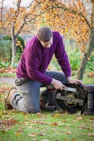 Using a brush to clean dirt and grass off mower blades before winter