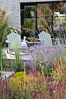 Sitting area on patio. Planting includes Echinacea purpurea, Salvia 'Caradonna', Rosmarinus officinalis - rosemary, Molinia caerulea subsp. arundinacea 'Windspiel', Allium and Perovskia atriplicifolia.