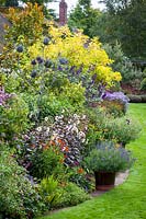 Autumn border in John Massey's garden with Salvia 'Amistad', dahlias, heleniums, helianthus and asters. Tall thistle sculpture.