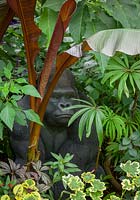 Tropical foliage border at John Massey's garden with gorilla sculpture. Includes Ensete maurelli - Ethiopian black banana, Begonia luxurians - Palm leaf begonia and variegated pelargonium