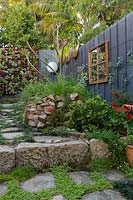 Inner city courtyard garden with framed mirror, sandstone raised bed and various plantings