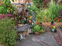 A gravel patio in front of a stone Bench with range of tropical planting including Canna's, Acer and Ricinus communis.