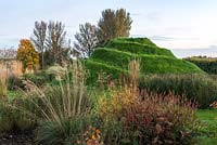 Mound, a grassy viewing platform, seen through beds of ornamental grasses and perennials.