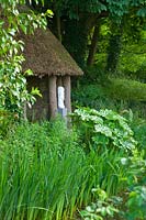 Woodland garden with thatched summerhouse and modern sculpture - Asthall Manor, Oxfordshire