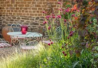  Small courtyard garden with Table and chairs, Stipa tenuissima, stone wall, Cirsium rivulare 'Atropurpureum', Cercis canadensis 'Ruby Falls'