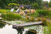 Natural swimming pool with waterlilies, marginal planting, wooden jetty and waterside seating area