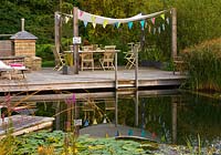 'natural' swimming pond with decking family eating area with shade canopy and bunting and outdoor oven and barbecue