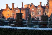 Formal topiary garden on frosty day winter with historic house in background
