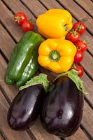 Colourful vegetables - Peppers, Tomatoes and Aubergines - outdoors on a wooden table