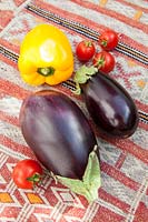 Colourful fresh vegetables - Aubergines, yellow pepper and cherry tomatoes on a kilim covered table