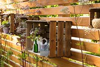 Decorative garden feature - wooden garden fence with ornamental wooden crate containing jug of cut flowers