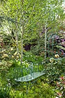 Spring woodland garden with 'Love' seat, white Narcissus (daffodil), and flowering Rhododendrons including R. 'Hotei'