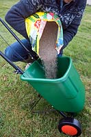 Pouring lawn fertilizer and weedkiller into a rotary lawn feed spreader