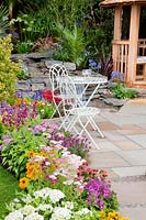 Patio in the perennial garden, iron garden furniture and wooden gazebo, waterfall in the background