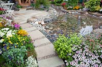 Patio with pond, perennial border and iron garden furniture