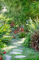 Stone walkway with Anigozanthos, Strelitzia, Phormium, Agapanthus, iron garden furniture in the background