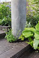 The Silent Pool Gin Garden, view of sunken garden with hostas against recycled concrete pillar, clay brick paving and corrugated metal fence – Designer: David Neale - Sponsor: Silent Pool Gin