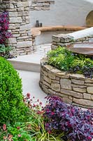 Miles Stone: The Kingston Maurward Garden, RHS Chelsea Flower Show 2019 - View over raised borders to a secluded seating area - Design: Michelle Brown, Sponsors: Miles Stone, Kingston Maurward College, Goulds Garden Centre, Greg and Will Wilkes Landscaping