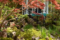 The Green Switch garden. Looking through the leaves of Acer palmatum 'Fireglow' and  Pinus to the summer house. Kazayuki Ishihara. Sponsor: G Lion