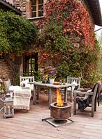 Garden table, chairs and fire basket on garden terrace set up for evening entertaining, Le Mas de BÃ©ty, France. 
