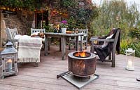 Garden table, chairs and fire basket on garden terrace set up for evening entertaining, Le Mas de BÃ©ty, France. 
