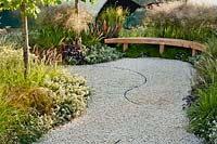 A curved gravel path and bench surrounded by soft planting including Lotus hirsutus, Sesleria autumnalis, Deschampsia cespitosa 'Goldtau', Astrantia 'Shaggy', Heuchera 'Palace Purple', Erigeron karvinskianus, Corylus colurna and Phormium tenax 'Platt's Black, The Between the Lines Garden, RHS Hampton Court Flower Show, 2013. 