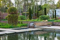 Garden pool with waterfall feature surrounded by formal topiary at Broughton Grange, Oxfordshire. 

