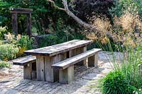 Chunky oak table and benches on a sunny terrace, Lower Treculliacks Farm, Falmouth, Cornwall, UK. 