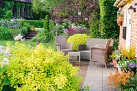 Seating area beside the back door of house, with mixed garden borders beyond, Terstan, Stockbridge, Hants, UK.  