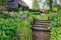 Brick steps lead between upper and lower garden, planted with beds planted with Buxus, hardy geraniums, Thalictrum aquilegiifolium, rosemary and alliums, Terstan, Stockbridge, Hants, UK